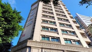 Un edificio de hotel alto con varios pisos, un reloj y un letrero que dice 'XINSHENG HOTEL'.