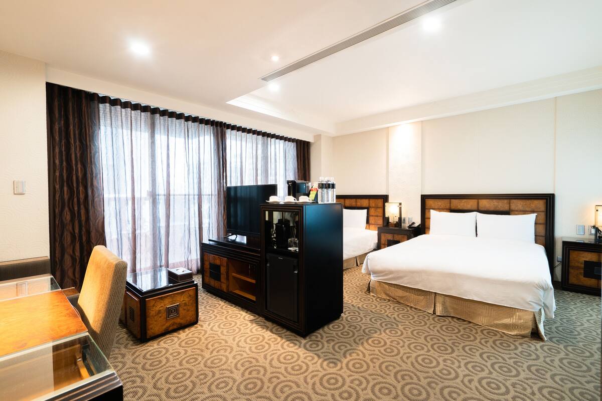 Habitación de hotel con una cama grande, un escritorio con silla, un minibar y un televisor.