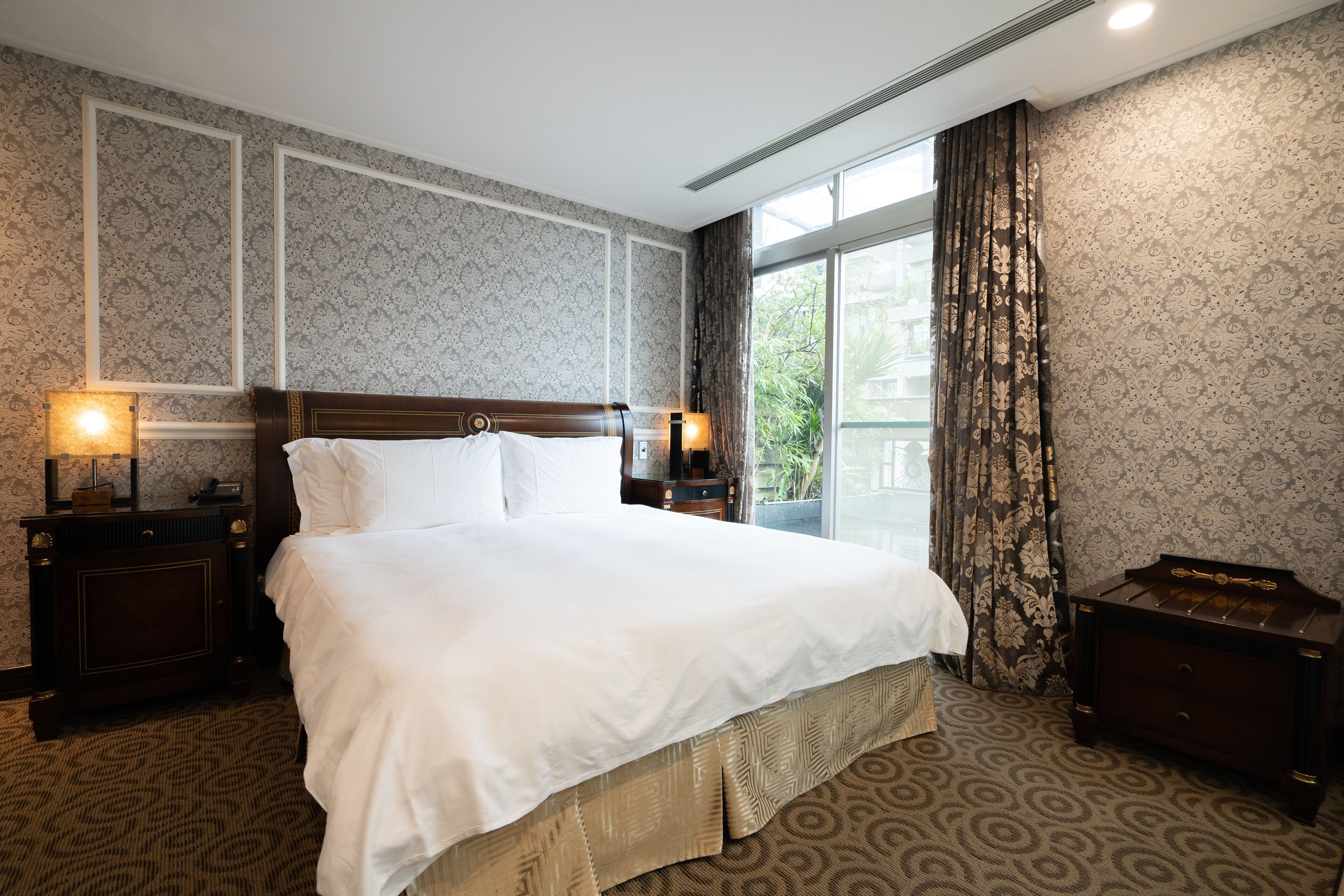 A hotel room with a large bed, two bedside tables with lamps, a dresser, and a window with curtains.