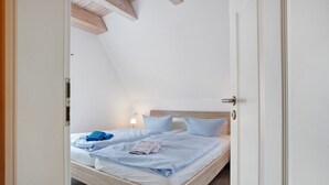 Een slaapkamer met een schuine kap, een houten bedframe, een bedlampje en een deur.