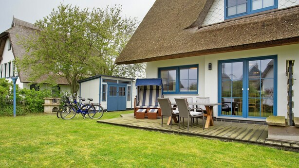 Een huis met rieten dak, een terras met tuinmeubilair en fietsen.