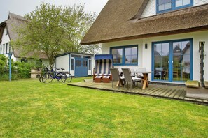 Une maison avec un toit de chaume, une terrasse avec des meubles d’extérieur et des vélos.