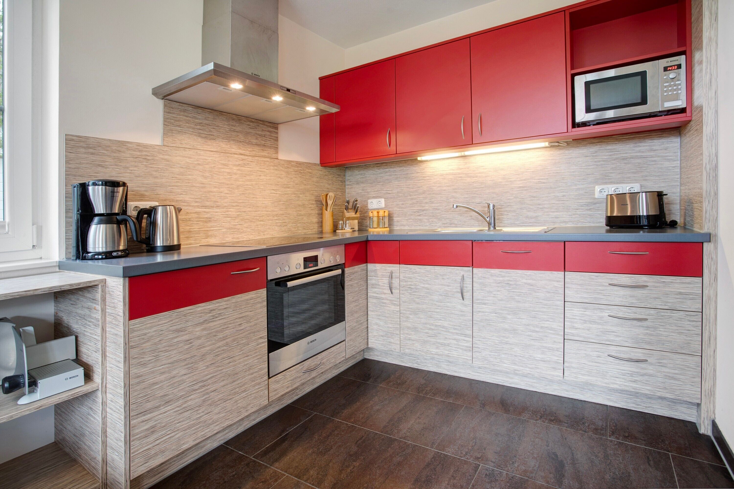 Una cocina moderna con armarios rojos, una cafetera de acero inoxidable, un microondas y un horno empotrado.