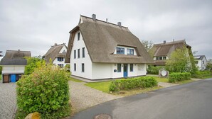 Een wit huis met rieten dak, een blauwe deur en een geplaveid oprit.