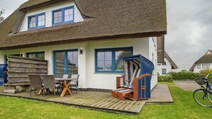 Une maison avec un toit de chaume, une terrasse en bois et du mobilier d’extérieur.