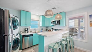 Una cocina moderna con armarios color esmeralda, electrodomésticos de acero inoxidable y una isla central con taburetes de bar.