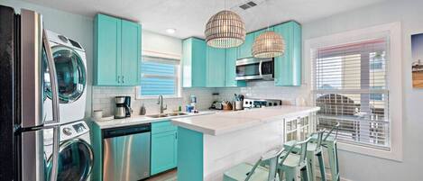 A modern kitchen with teal cabinetry, stainless steel appliances, and a central island with bar stools.