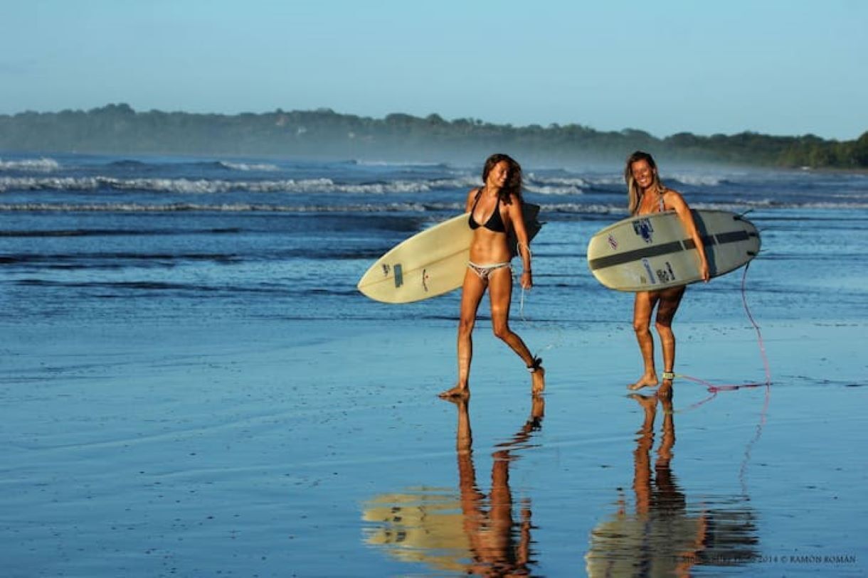 Deux personnes se promènent sur une plage, portant des planches de surf.