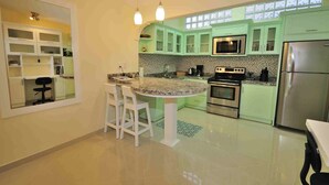 A modern kitchen with green cabinets, a central island, white bar stools, stainless steel appliances, and a large window providing natural light. - Newly Renovated Condo One Block From Beach (Buenos Aires)