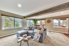 Amplia sala de estar con un sofá seccional, ventanas grandes, una viga de techo de madera y vistas a una terraza.