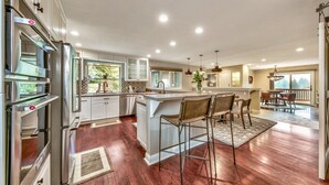 A modern kitchen with stainless steel appliances, a central island with bar stools, and a dining area with a view.