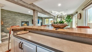 A modern kitchen with a large island, stone wall, and a fireplace.