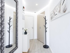 A hallway with a coat rack, a mirror, and a door leading to a room.