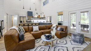 A spacious living room with a brown leather sectional sofa, a round coffee table, and a patterned rug. - Stunning Modern Cabin (Broken Bow)