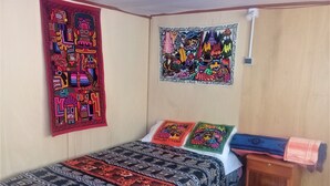 A bedroom with a bed, two pillows, a wall hanging, and a small wooden cabinet.
