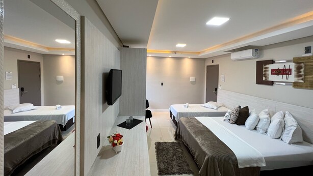 A modern hotel room with two beds, a flat-screen TV, a small table with a vase of flowers, and a mirror. - Hotel Balneário do Parque (Penha)