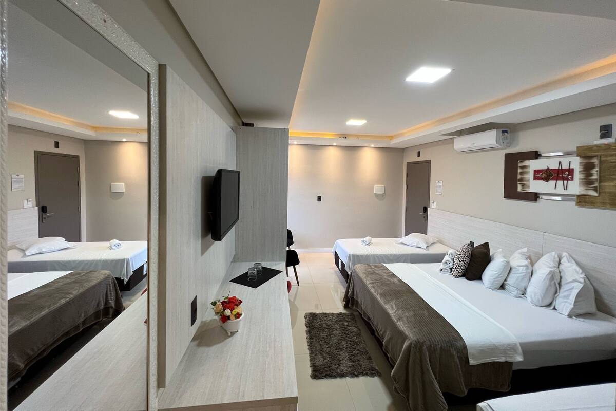 A modern hotel room with two beds, a flat-screen TV, a small table with a vase of flowers, and a mirror.