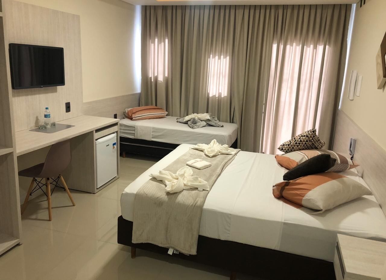 A hotel room with a bed, a desk, a chair, a TV, and a window with curtains.