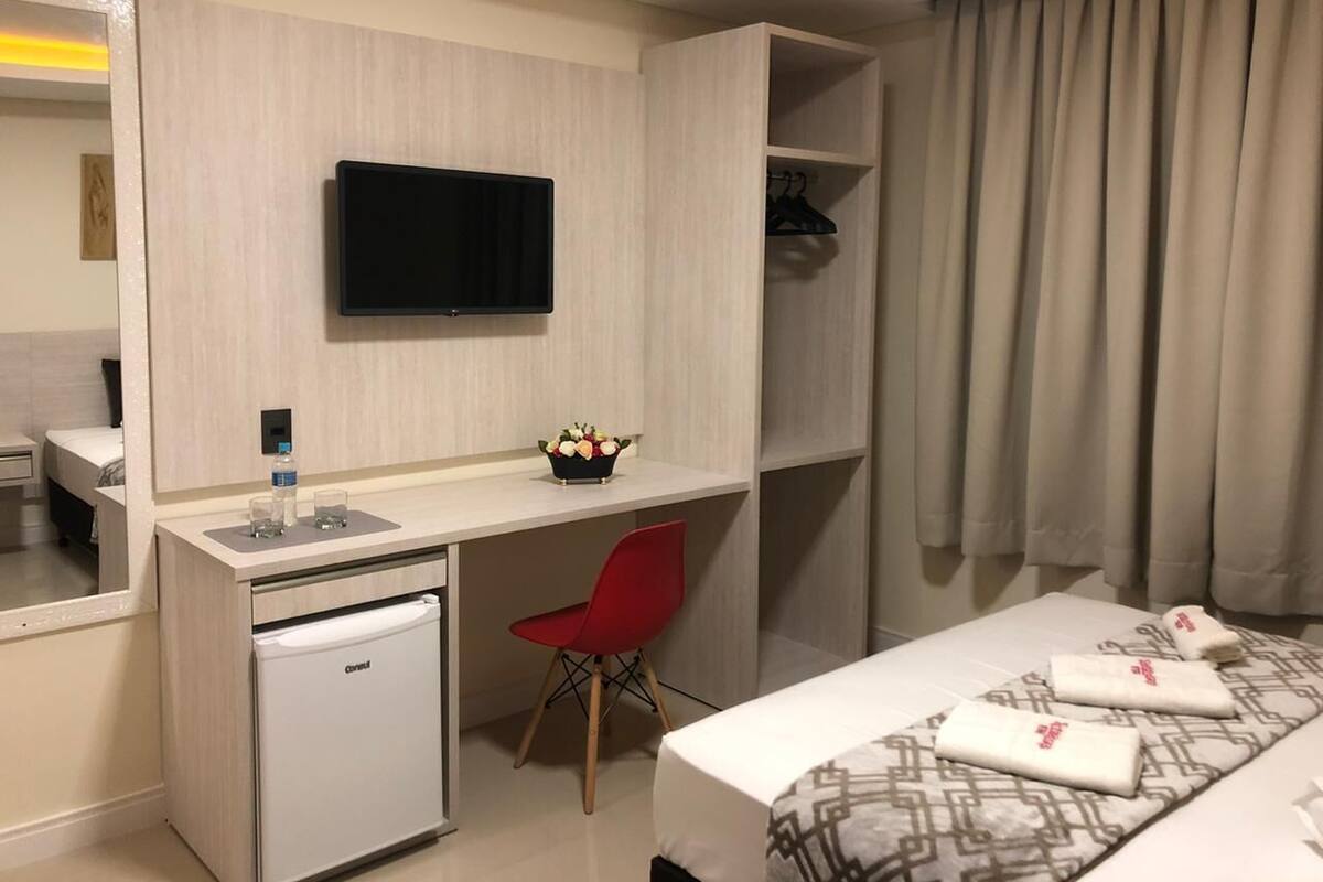 A hotel room with a bed, a desk, a small fridge, a TV, and a mirror.