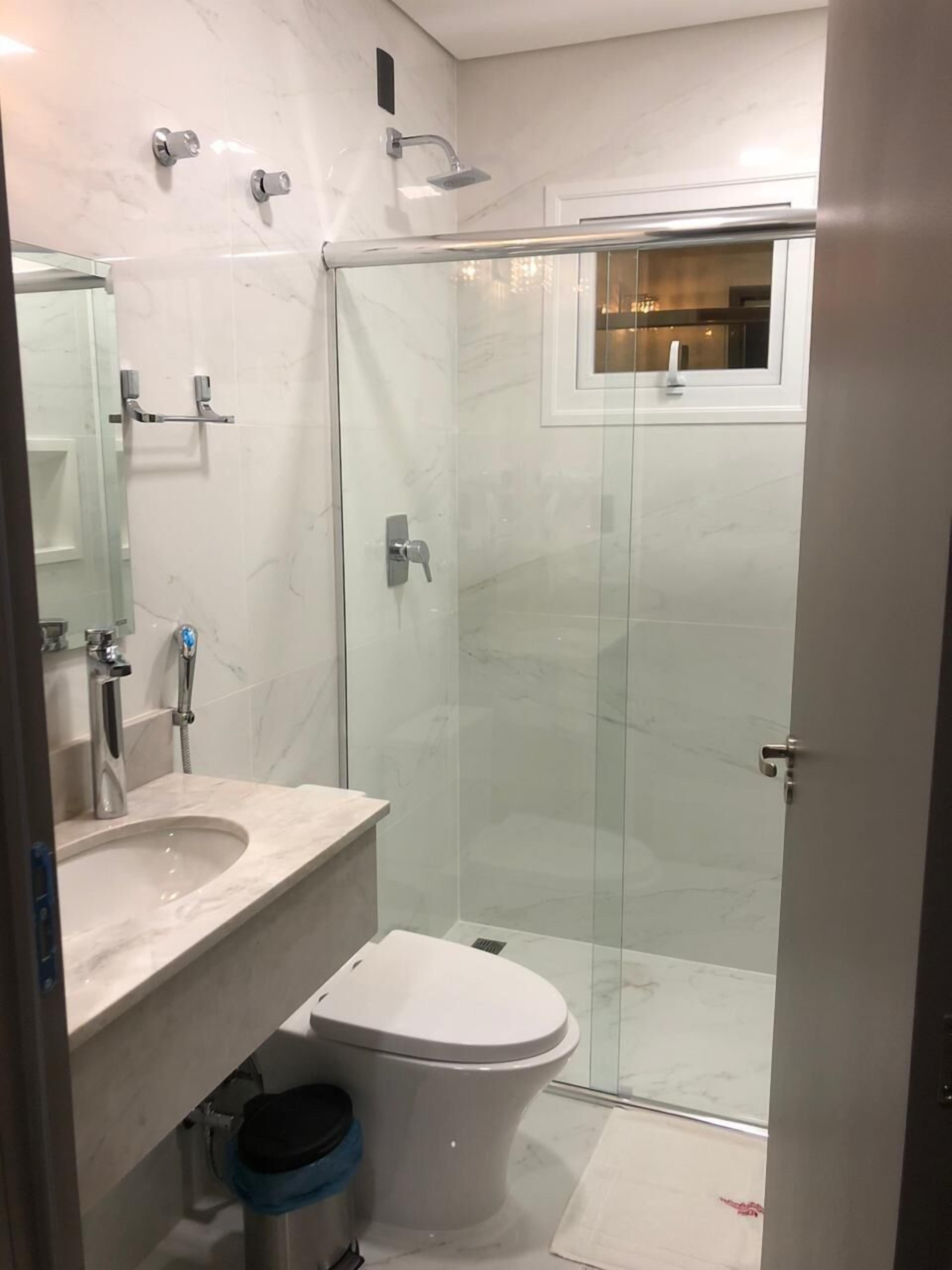 A modern bathroom with a glass-enclosed shower, a white sink, and a toilet.
