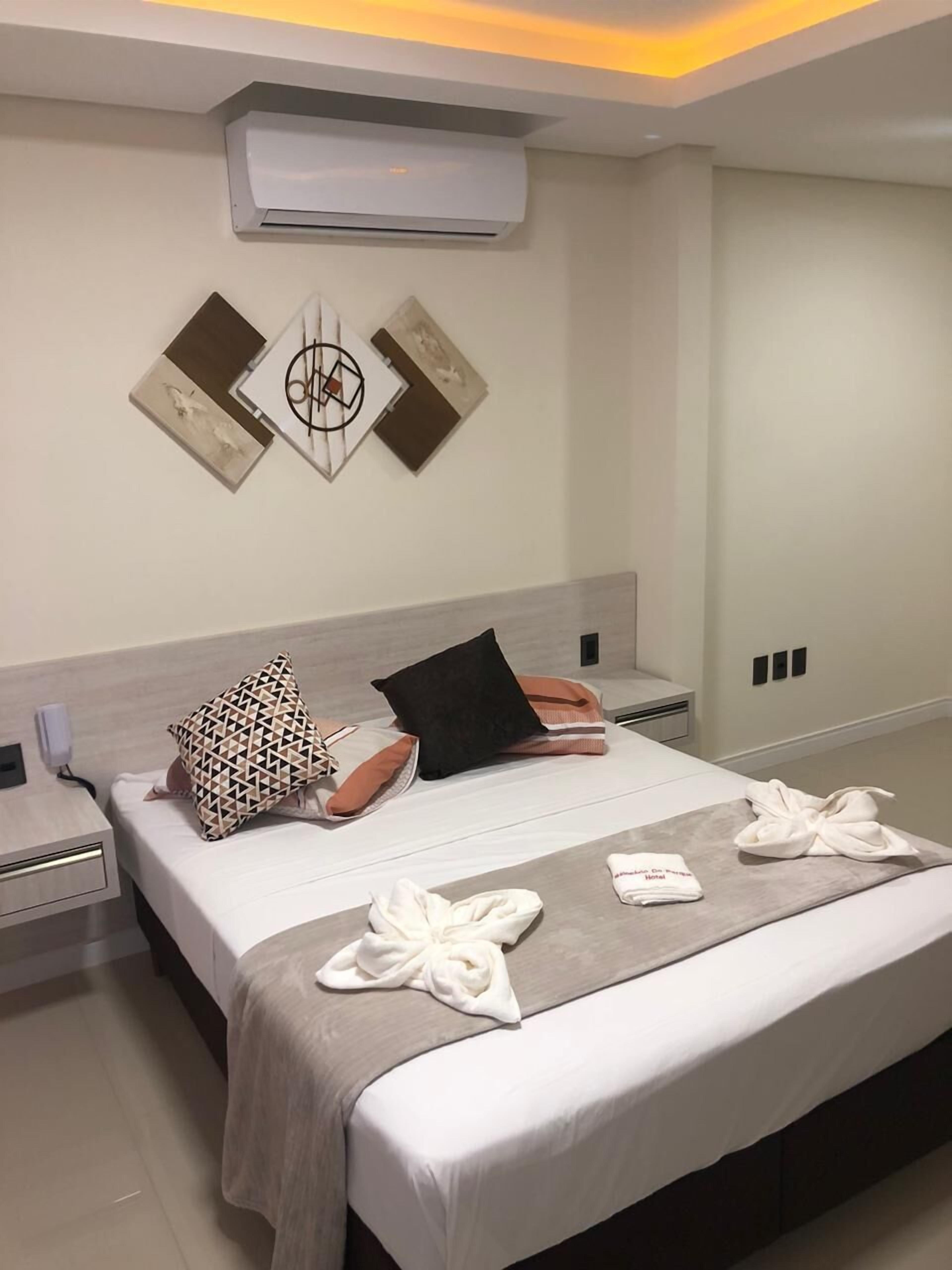 Une chambre d’hôtel moderne avec un lit soigneusement fait, un climatiseur fixé au mur et un décor minimaliste.