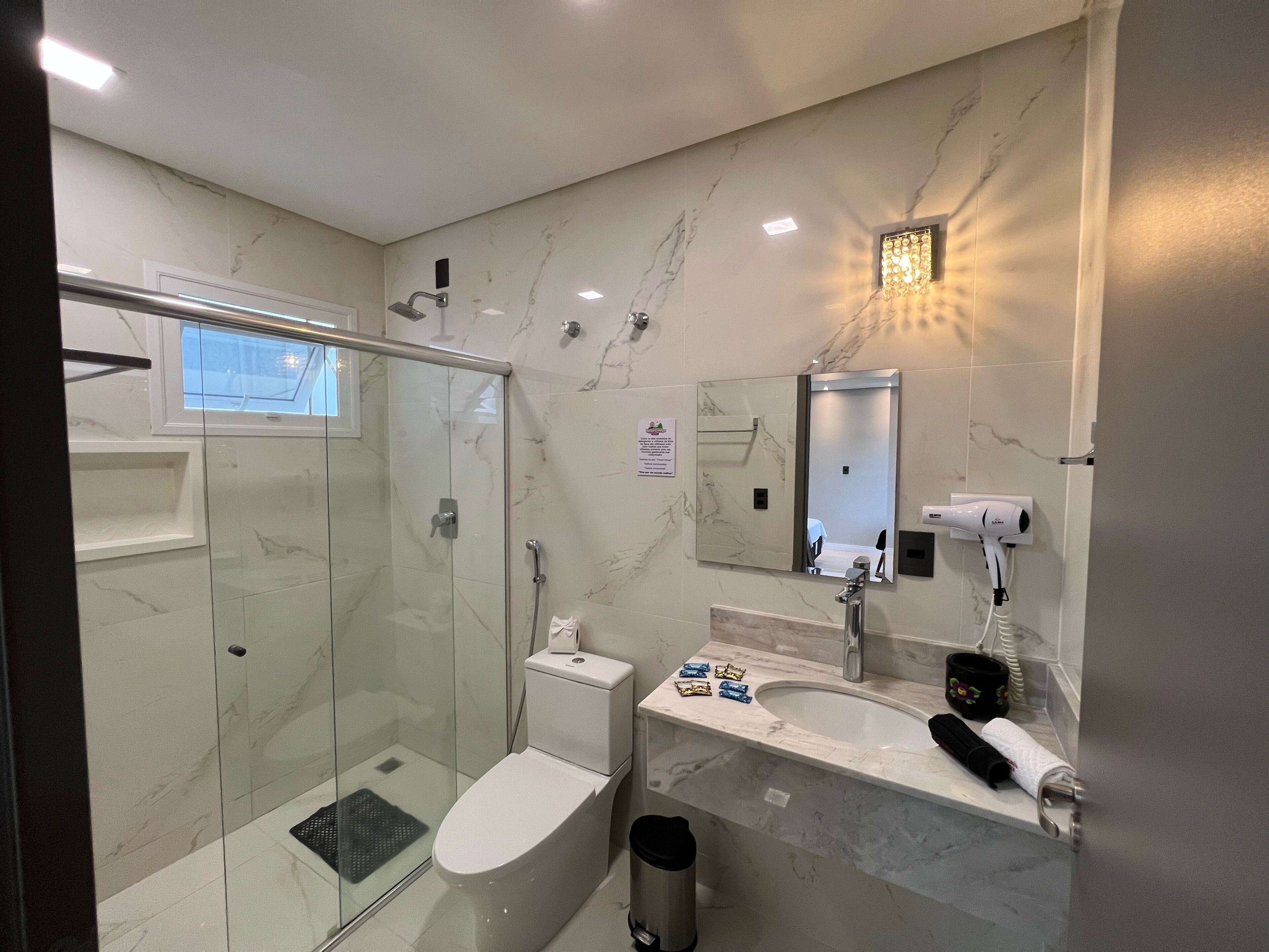 Un baño moderno con cabina de ducha de vidrio, inodoro, lavabo con espejo y secador de pelo en la encimera.
