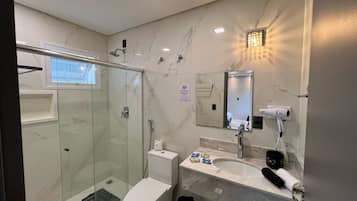 Un baño moderno con cabina de ducha de vidrio, inodoro, lavabo con espejo y secador de pelo en la encimera.