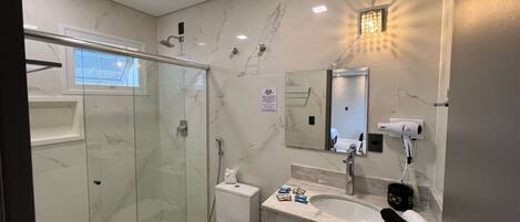 Un baño moderno con cabina de ducha de vidrio, inodoro, lavabo con espejo y secador de pelo en la encimera.