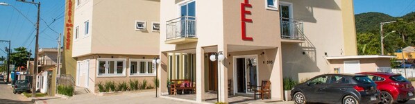 A two-story building with a balcony on the second floor, a visible entrance, and a parking area with cars. - Hotel Balneário do Parque (Penha)