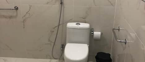 A bathroom with a toilet, shower, and handrail.