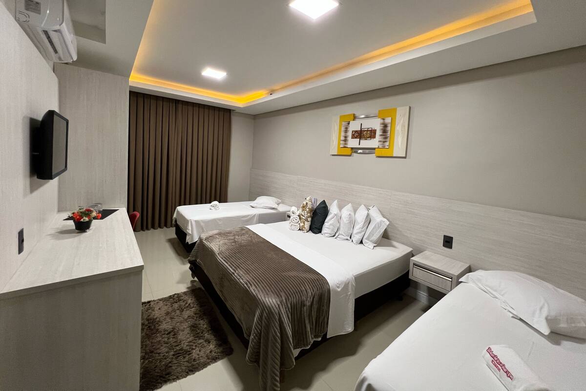 A hotel room with two beds, a desk with a flat-screen TV, a wall-mounted air conditioner, and a ceiling light fixture.