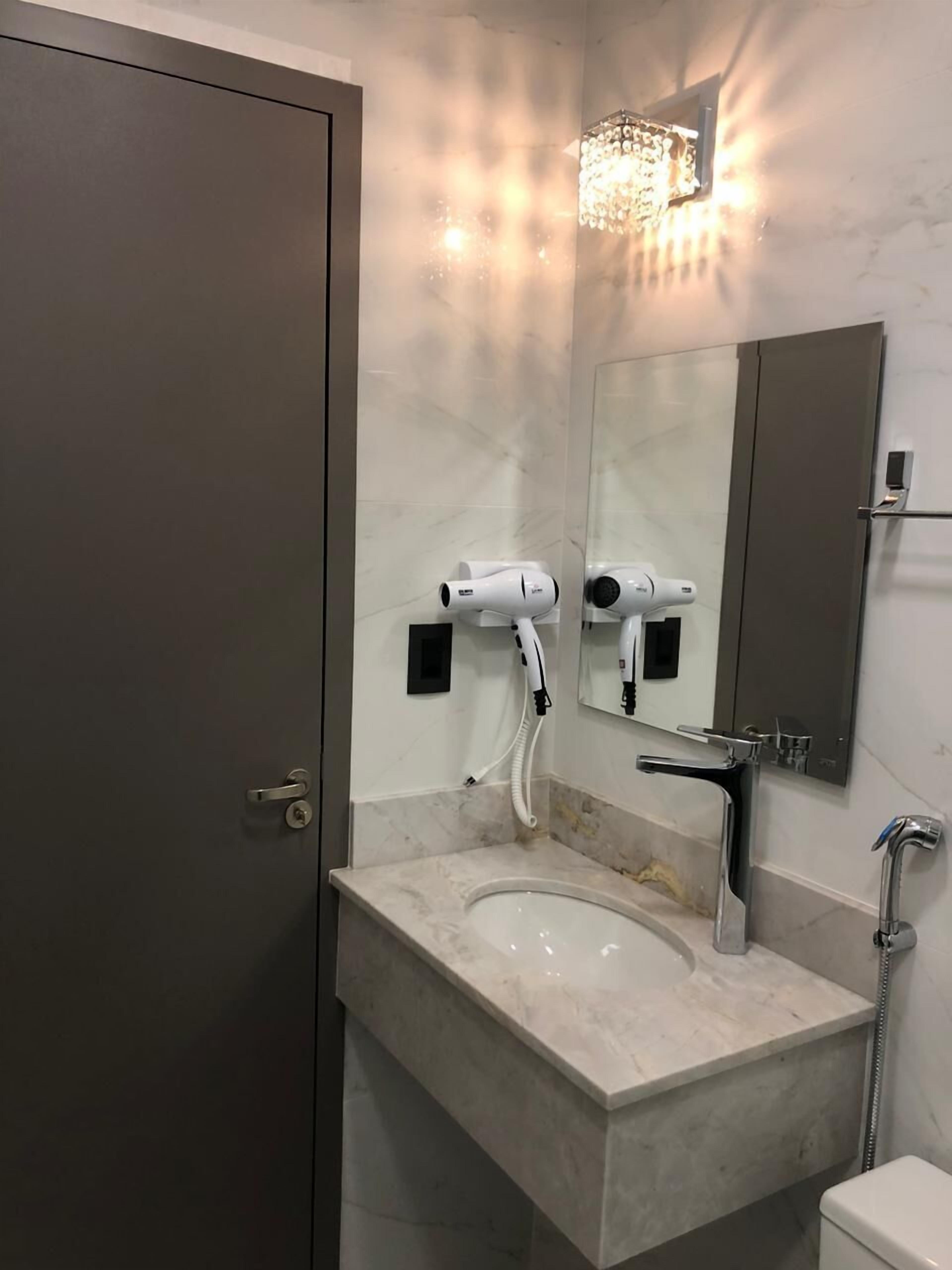 Un baño con lavamanos de mármol, espejo, secador de pelo y ducha.
