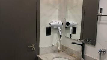 Un baño con lavamanos de mármol, espejo, secador de pelo y ducha.