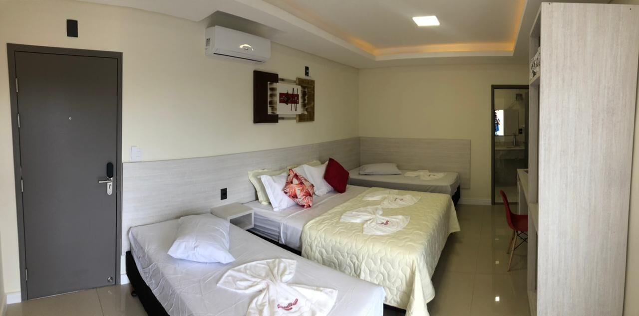 A hotel room with three beds, a door, an air conditioning unit, and a mirror.