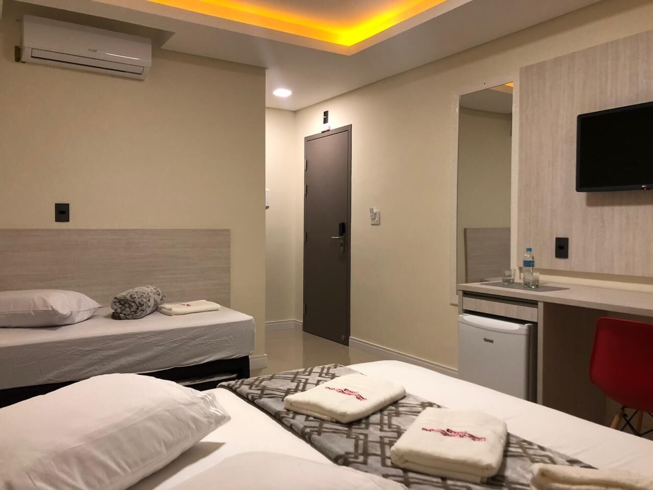 Habitación de hotel con dos camas, un escritorio con silla, televisión y minibar.