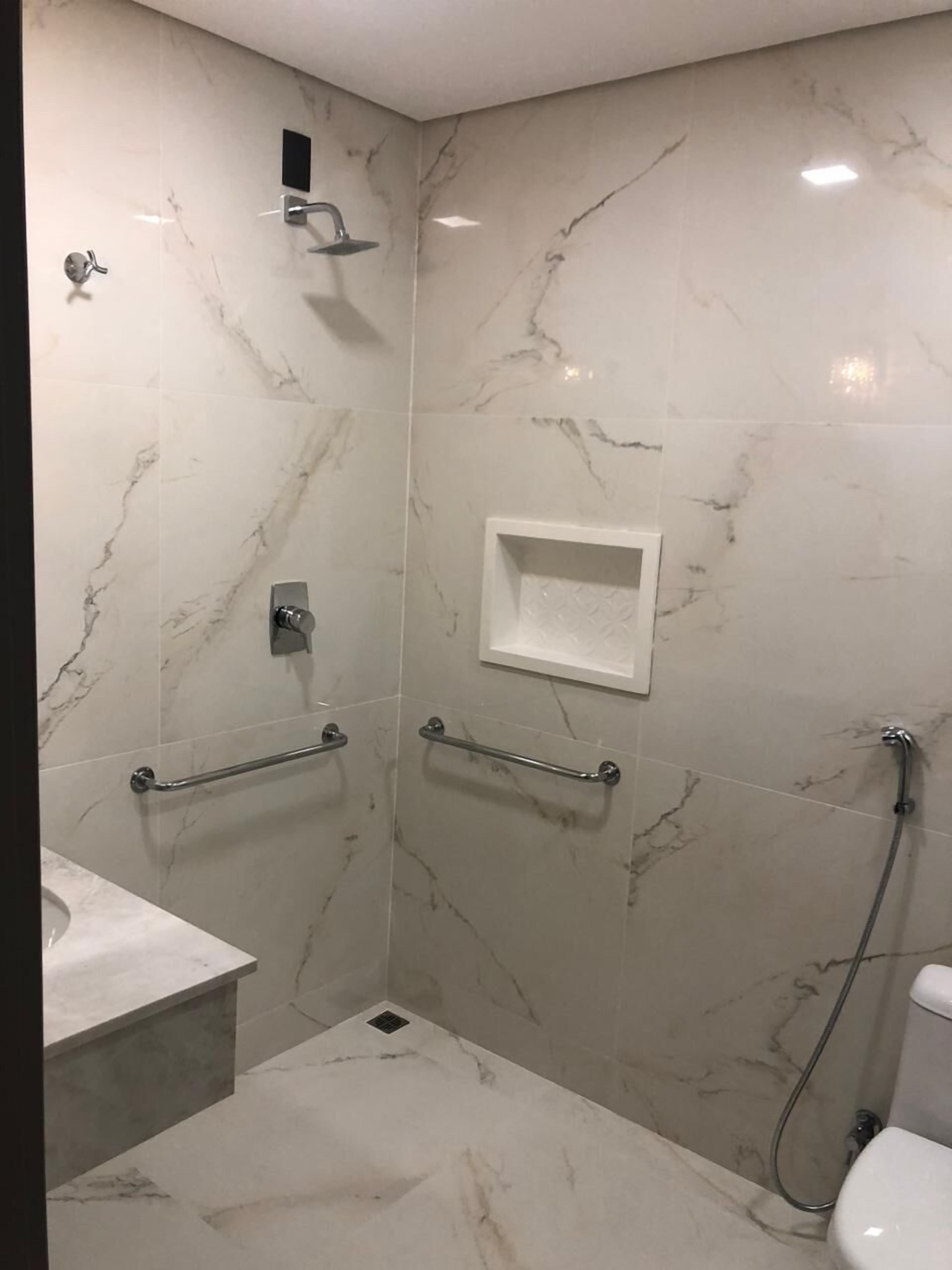 A bathroom with marble walls, a shower, a toilet, and a sink.