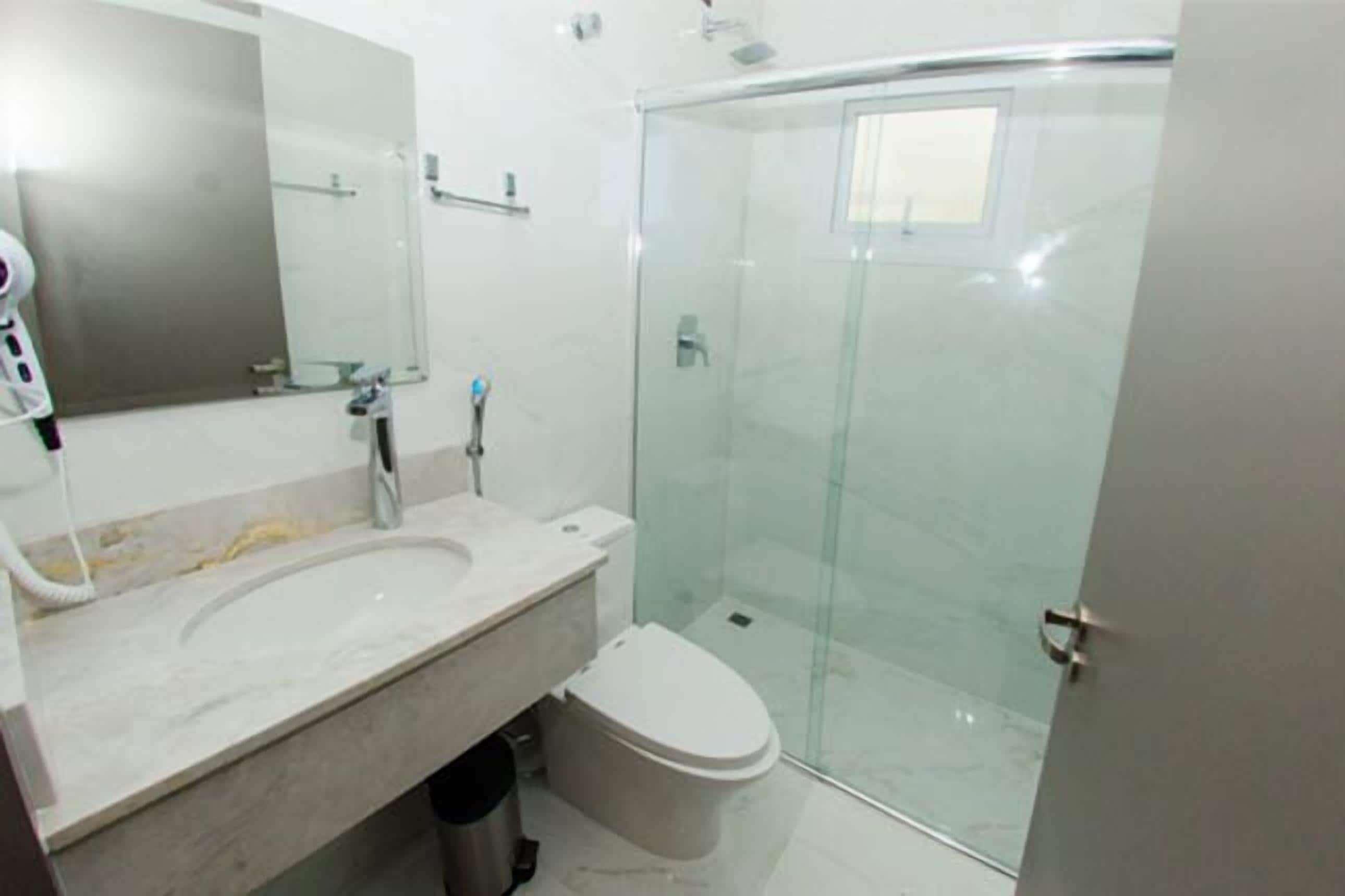 A modern bathroom with a glass shower enclosure, a marble sink, and a toilet.