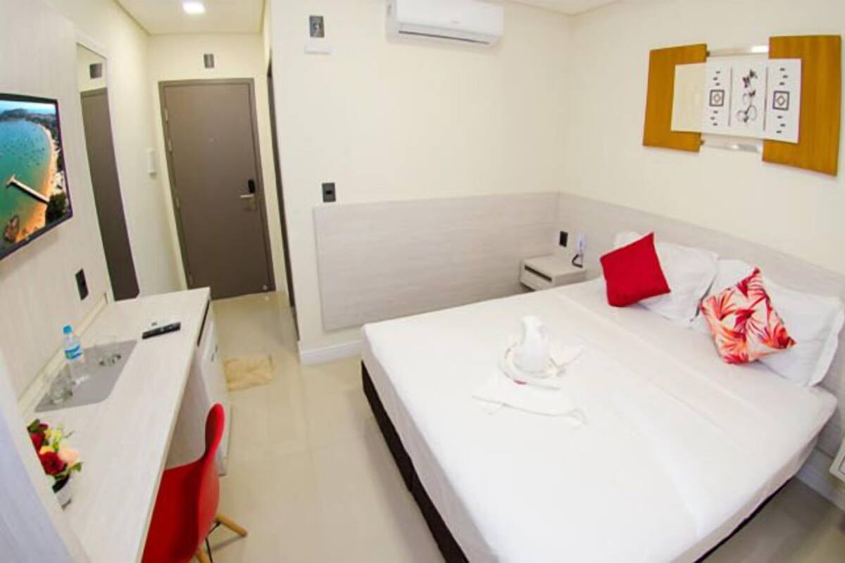 A hotel room with a bed, a desk, a chair, a nightstand, and a wall-mounted TV.