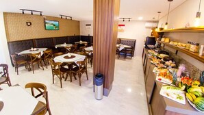A restaurant with round tables and chairs, a buffet area with various food items, and a television mounted on the wall. - Hotel Balneário do Parque (Penha)