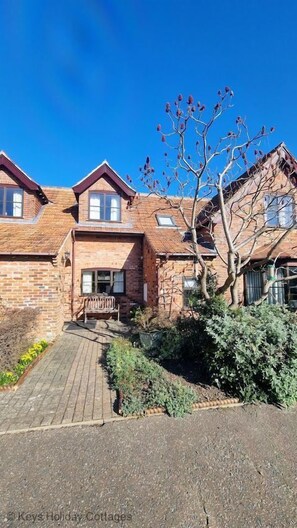 A two-story brick house with a wooden deck and a tree in the front yard.