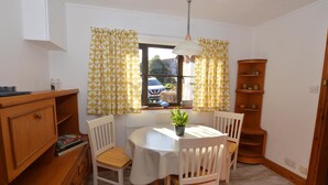 A dining area with a round table, white chairs, a potted plant, and a wooden bookshelf.