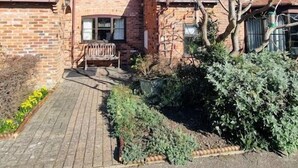 A two-story brick house with a wooden deck and a tree in the front yard.