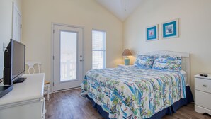 Quarto com cama, escrivaninha com computador, cadeira, mesa de cabeceira e duas imagens emolduradas na parede.