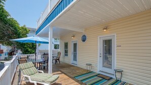 Um deck coberto ao ar livre com espreguiçadeiras, uma mesa e um guarda-sol azul.