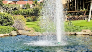 A fountain in a landscaped area with palm trees and a building in the background. - Maui South Kihei New Modern Spacious Ocean View Condo, 5 mins walk to beach! (KIHEI)