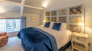 Une chambre à coucher avec un grand lit, une table de chevet, une chaise et une fenêtre avec des rideaux.