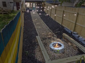 A backyard with a fire pit, wooden fence, and string lights. - 2 Bedroom Townhouse Fire Pit - BBQ - Fun Relax (Mableton)