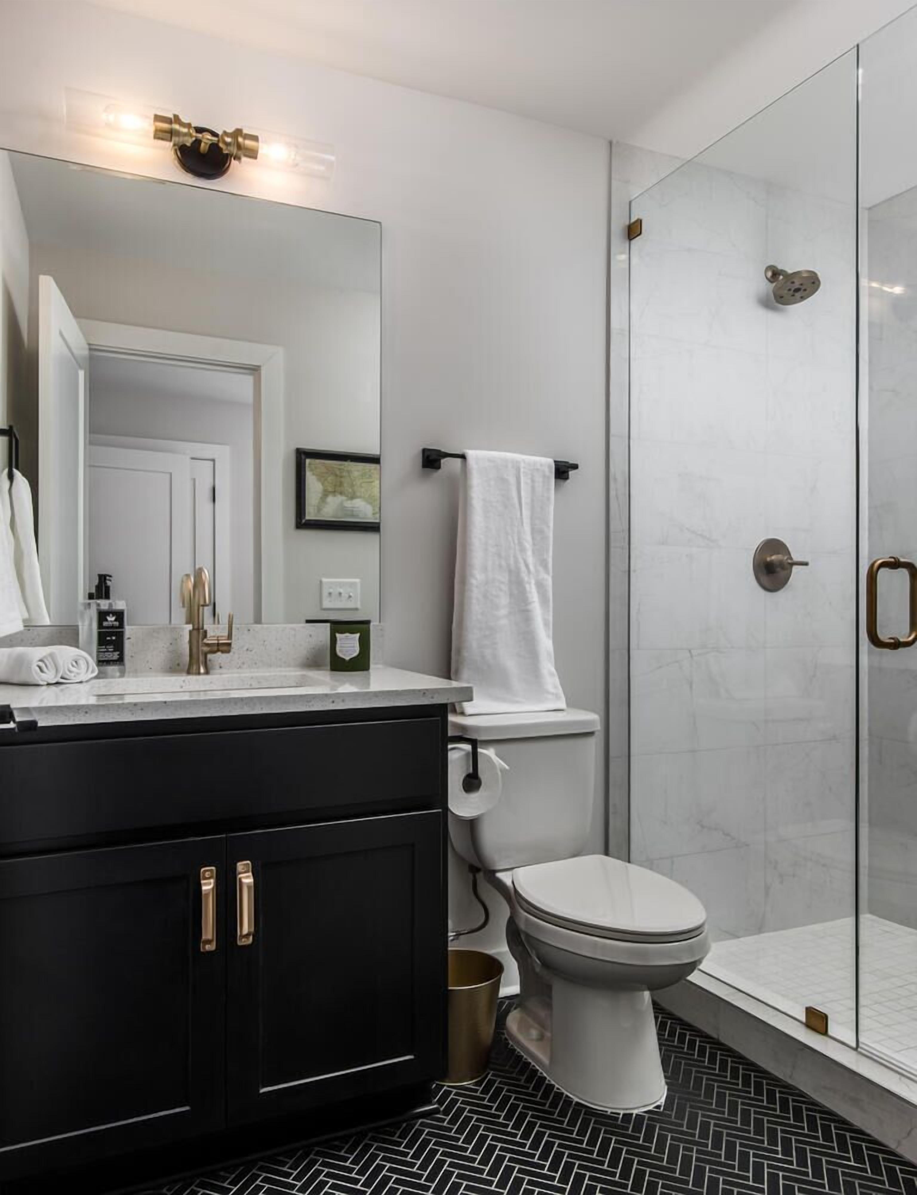 Une salle de bain moderne avec une douche à l’italienne en verre, des toilettes blanches et un meuble-lavabo noir doté de poignées dorées.