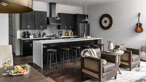 Una cocina moderna con armarios oscuros, una isla central, taburetes de bar y una zona de comedor con mesa lista para comer.