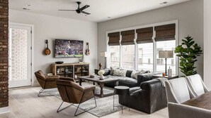 A spacious living room with a sofa, chairs, a coffee table, and a television. - Urban Row - Rooftop Hot Tub - Heart of Gulch (Nashville)